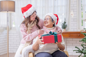 A young woman gives a red gift box to an older woman for Christmas