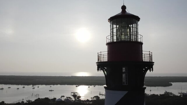 Aerial view of the silhouette of the St. Augustine Lighthouse against the bright sun and ocean, boats dotting the water, St. Augustine, Florida, United States.