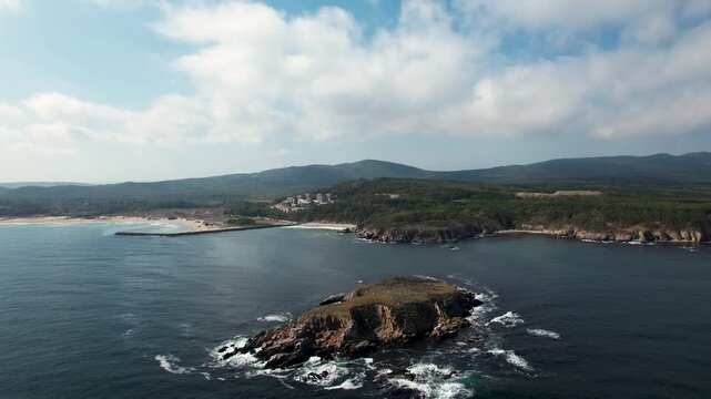 Aerial view of the rocky Saint-Thomas Island near Arkutino beach where the dark blue sea meets the green forest under a blue sky, Arkutino, Primorsko, Bulgaria.