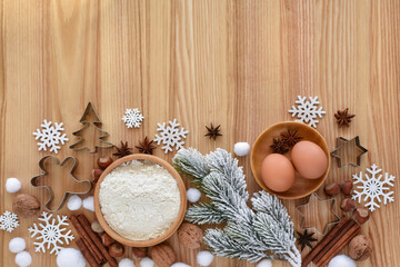 Composition with a snowy spruce branch, flour, eggs, and festive cookie cutters on a wooden table