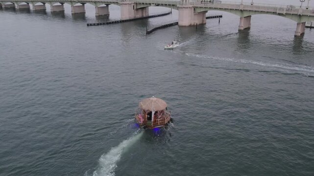 Aerial view of the Bridge of Lions over the water as a tiki hut boat passes underneath, creating a dynamic scene, St. Augustine, Florida, United States.