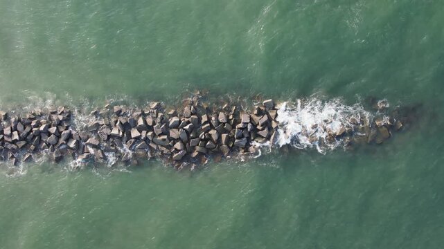Aerial view of a rock breakwater, a dark line against the turquoise ocean, with foamy waves crashing over it, St. Augustine, Florida, United States.