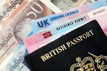 Obraz premium United Kingdom driving license with passport and residence permit card on UK money close up