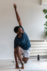 Fit man stretching on a yoga mat at home, performing a side bend exercise after workout in a bright...
