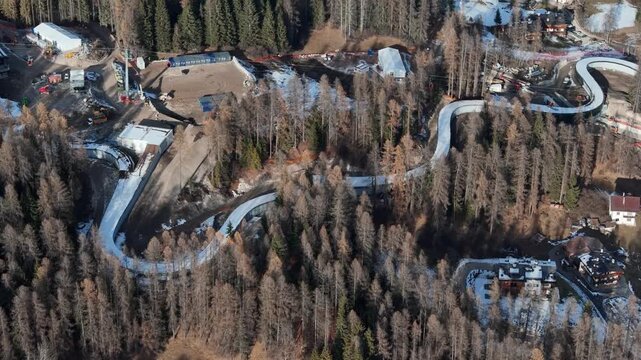 Aerial view of the Cortina Sliding Centre winding through a dense forest, contrasting the white track against the muted tones, Cortina d'Ampezzo, Veneto, Italy.