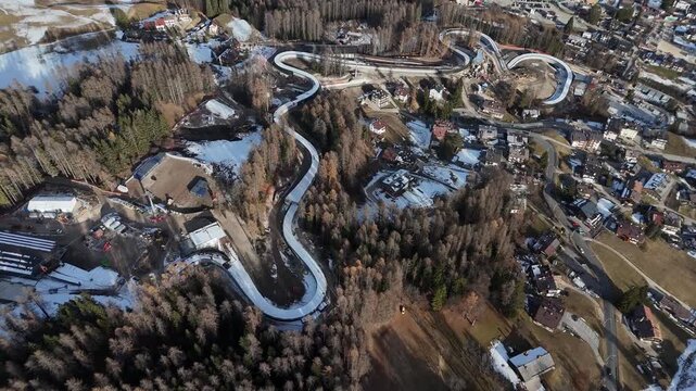 Aerial view of the winding Cortina Sliding Centre, contrasting the stark white track against the surrounding trees, Cortina d'Ampezzo, Veneto, Italy.
