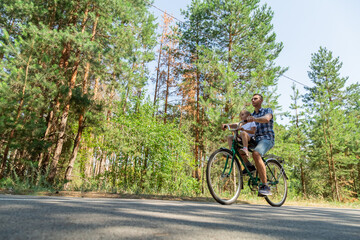 A young father carries his little daughter in a bicycle seat. Dad and child ride a bike in forest