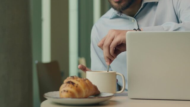 Indian ethnic Muslim businessman specialist with laptop business man mixing tea mix sugar in coffee male guy Arabian executive leader with computer enjoying lunch breakfast distant job in restaurant