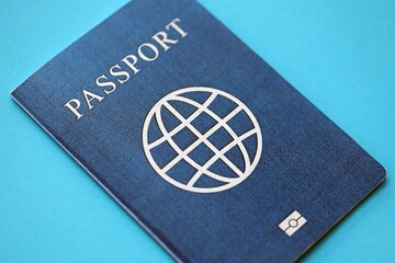 Generic passport book on light blue paper background close up. Travel document on blue surface