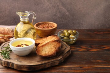 Slices of baguette with oil, spices and olives on wooden table, closeup. Space for text