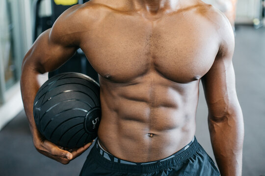 Muscular man holding medicine ball in gym. Close-up of a muscular athletic man holding a medicine ball during strength training workout in a gym.
