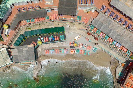 Aerial view of sun-soaked beach with colorful umbrellas and neatly arranged lounge chairs meeting the turquoise waters near the iconic cliffs, Capri, Campania, Italy.
