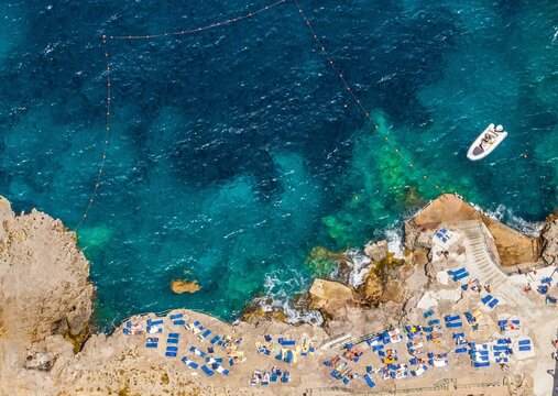 Aerial view of the coastline meeting the turquoise sea, sunbeds dotting the rocky shore near Marina Piccola, a boat bobbing gently in the bay, Capri, Campania, Italy.