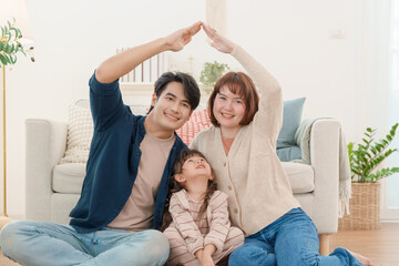 Happy Asian family making roof shape with hands over daughter head sitting on floor at home real estate insurance and protection concept