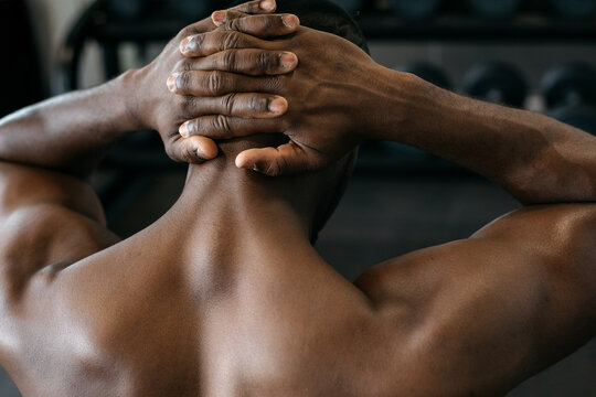 Close up of a muscular man flexing his muscles. Shirtless African American athlete stretching shoulders and upper back muscles during gym workout.