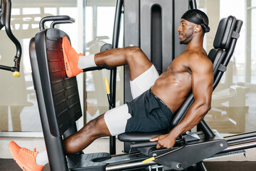 Athletic man using leg press machine for leg workout. Fit man performing leg press exercise with...