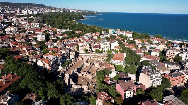 Aerial view of the ancient Roman Thermae ruins contrasting with modern buildings, lush greenery, and the deep blue sea, Varna, Varna, Bulgaria.