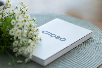 New Testament book on a table with a bouquet of white flowers. Holly Bible.