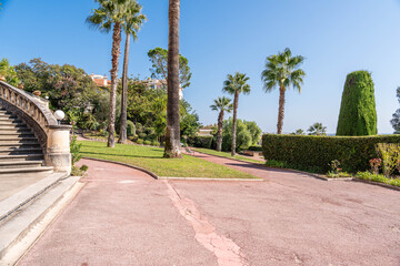 Obraz premium Mediterranean garden walkway with palm trees, manicured greenery and classic architecture on sunny day