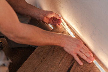 Person Installs Lighting Under Wooden Shelf in Indoor Space During Daylight