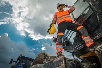 Worker Stands on Machinery and Talks on Phone at Construction Site in Day