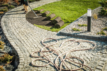 Gardener Works on Lawn With Tools Near Cobblestone Path in the Afternoon