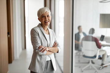 Confident Senior Woman in Grey Blazer Standing in Modern Office Hallway