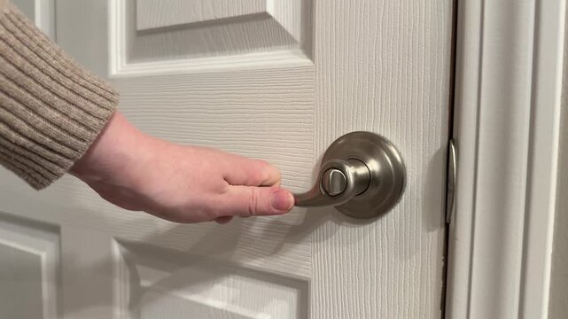 Close up of a woman&rsquo;s hand jiggling an interior door handle to check if the door is locked. Subtle home security, privacy, and safety concept inside a house.