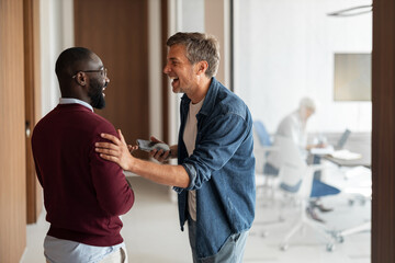 Fototapeta premium Friendly Office Encounter Between Colleagues: Laughing Handshake in the Hallway