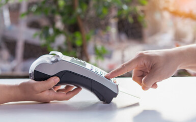 close-up of two hands using a payment terminal for a card transaction. One hand holds the card reader while the other presses a button on the keypad.
