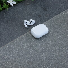 Wireless earbuds and charging case on concrete surface outdoors with minimal style