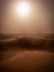 A desert landscape with sand dunes under a bright sun and hazy sky.