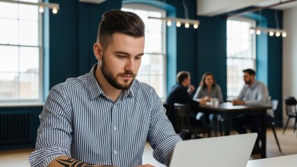 Focused young businessman working on laptop in modern office. Professional male entrepreneur using technology in a contemporary coworking space.