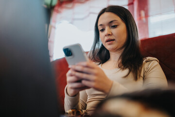 A young woman sits on a red couch indoors, focused on her smartphone screen in a casual, relaxed setting.