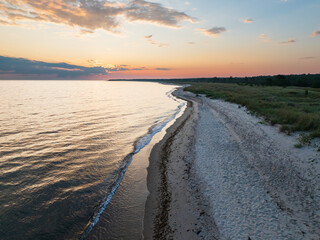 Aerial scenic view of sandy beach and Baltic sea coastline in Estonia during a beautiful golden sunset with colorful sky.
