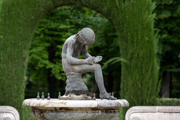 Bronze statue of a contemplative boy in a garden fountain