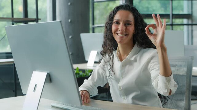 Ethnic Hispanic Arabian business woman showing ok sign gesture in office typing computer businesswoman female girl using pc service online software recommend approve cyberspace corporate technology