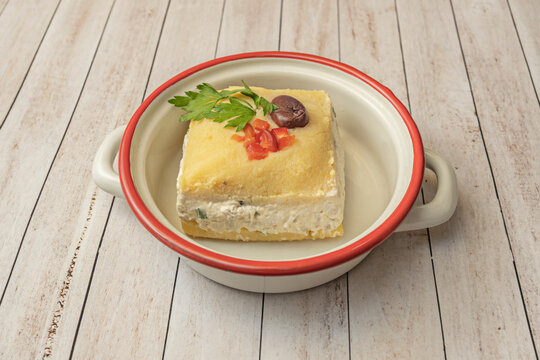 Causa rellena (stuffed causa) filled with shredded chicken in a creamy aji amarillo sauce, molded into a circular shape and adorned with thin slices of avocado, toasted corn, and a sprig of cilantro