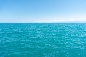 Obraz premium A vast expanse of vibrant turquoise blue water under a clear, bright blue sky, with a subtle horizon line and faint distant mountains.