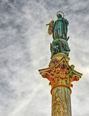 Fototapeta premium Low-angle view of the Column of the Immaculate Conception in Rome, Italy, featuring the bronze statue of the Virgin Mary atop an ornate Corinthian marble column beneath dramatic clouds. Located in Pia