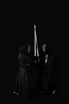 Professional kendo athlete in uniform posing with shinai sword in black and white