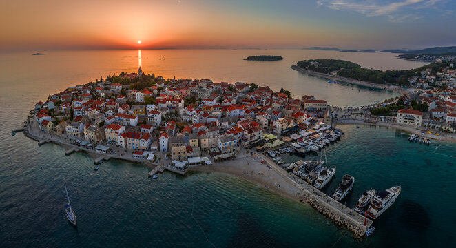 Primosten, Croatia - Aerial panoramic view of Primosten peninsula and old town on a sunny summer afternoon in Dalmatia. Yacht marina, sailboats, setting sun, golden sky at sunset by the Adriatic