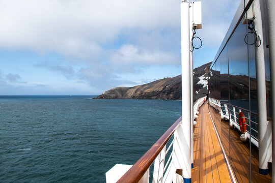 View of the dark, rippling ocean contrasting with the light, textured clouds from the wooden deck of a ship, with a distant landmass, Deception Island, Antarctica.