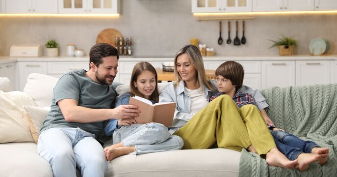Happy family reading book and spending time together on sofa in kitchen at home - Powered by Adobe