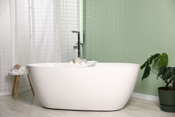 Fototapeta premium Tub, folding screen and green houseplant in bathroom. Interior design