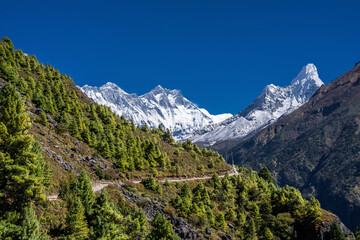 Fototapeta premium Snowy Lhotse and Ama Dablam peaks behind the mountainside and trekking route from Namche bazar to Tengboche. Everest base camp trek in Nepal.
