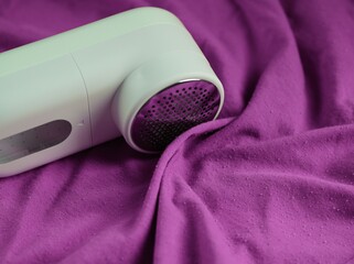 A portable lint remover lying on a purple clothes. Close-up