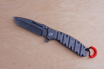 Dark gray everyday carry EDC pocket knife is displayed open on a neutral wooden tabletop, emphasizing its robust construction and aggressive aesthetic.