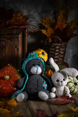 Knitted toys. A bear and a hare on a wooden table surrounded by autumn leaves and pumpkins.