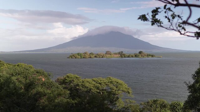 View shows Concepcion volcano on Ometepe island in Nicaragua from a distance with trees and lake visible in the foreground